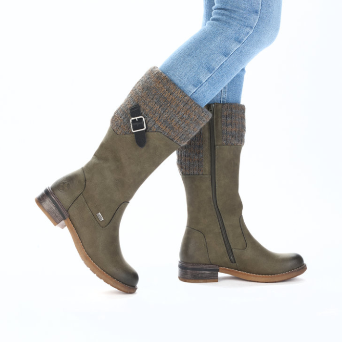 Green knee-high boots with patterned cuffs worn with blue jeans.