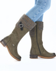 Green knee-high boots with patterned cuffs worn with blue jeans.