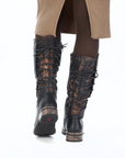 Black knee-high boots with lace-up design worn by a person in brown leggings and tan ribbed dress.