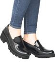 Legs in jeans wearing black leather penny loafer with platform heel.