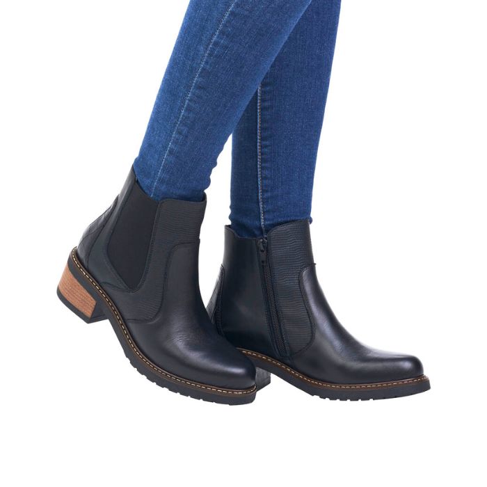 Legs in jeans wearing black leather Chelsea boot with brown stacked heel.