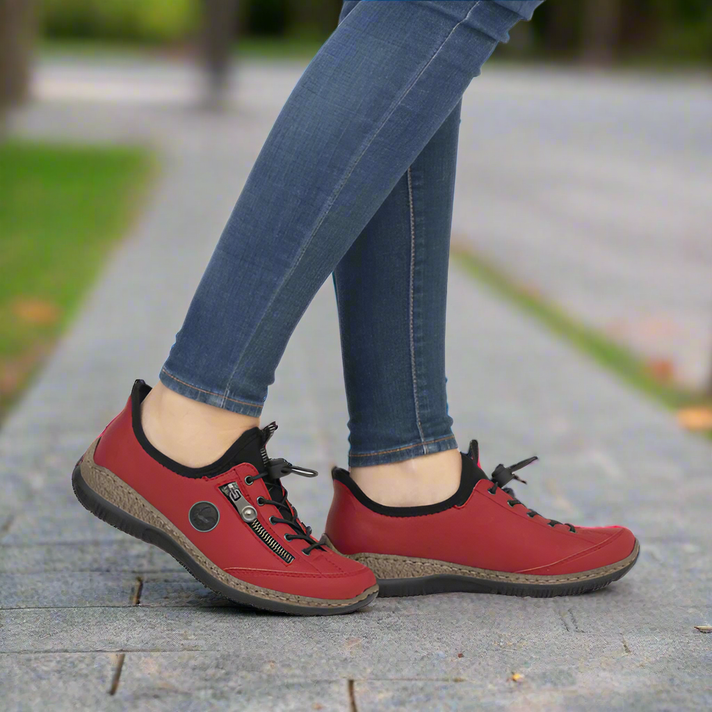 Red casual shoes worn with blue jeans on a blurred outdoor background.