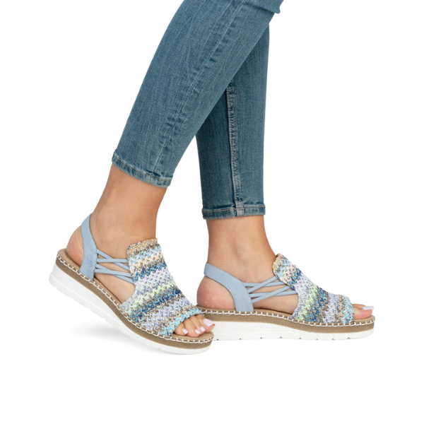 Model wearing pastel blue Women&#39;s Rieker V1241 Backstrap Sandals with jeans, showcasing comfort fit, colorful knit design, and flexible sole.
