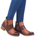 Legs in jeans wearing light and dark brown patched ankle boot with stacked heel and outside zipper.