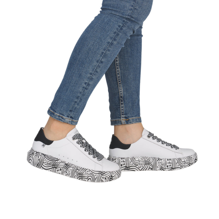White sneakers with black patterned midesole worn with blue jeans.