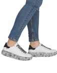 White sneakers with black patterned midesole worn with blue jeans.