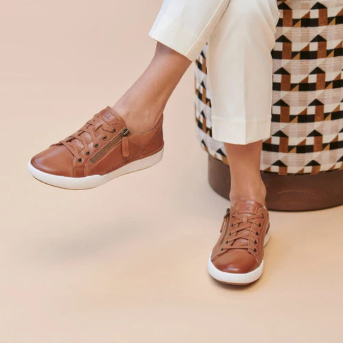 Brown sneakers worn with white pants sitting on patterned stool.