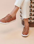 Brown sneakers worn with white pants sitting on patterned stool.