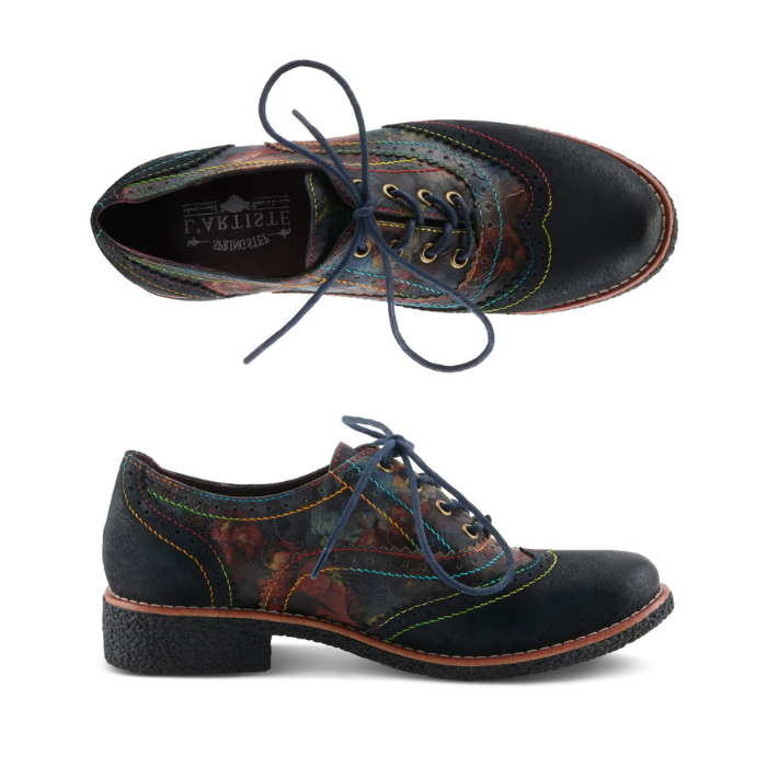 A pair of Oxford shoes with dark navy toe cap and heel, a painterly floral patterned leather upper in red, orange, green, and blue tones, blue waxed laces and rainbow stitching accents.