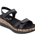 A black wedge sandal with black Velcro straps, black Remonte logo'd footbed, a faux- cork-textured midsole and black platform outsole.