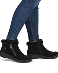 Black ankle boots with faux fur trim and a side zipper, shown on a model wearing blue jeans.