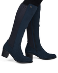A pair of knee-high boot in dark navy blue suede, with a low block heel worn by woman in black jeans