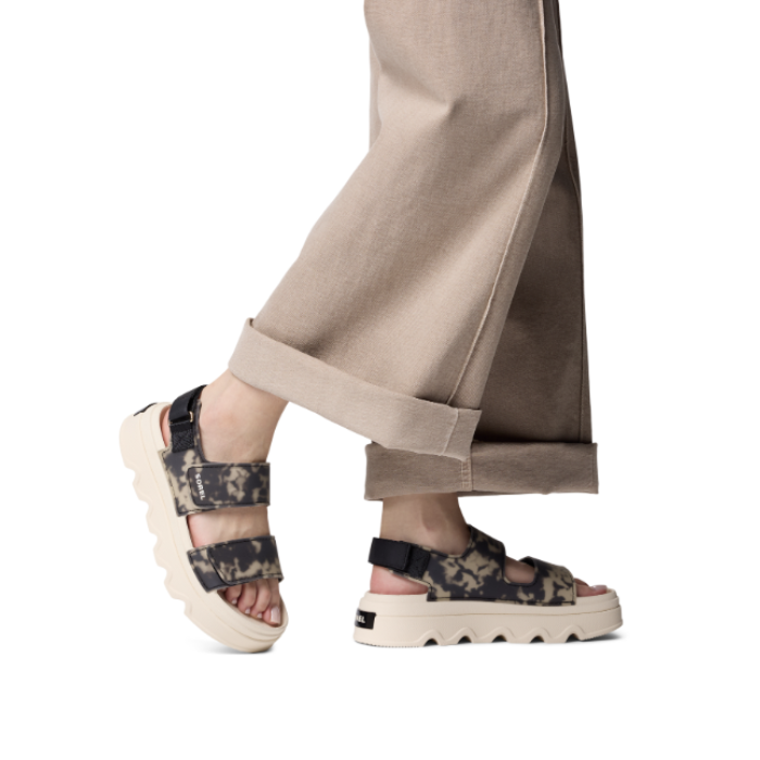 Camouflage-patterned platform sandals worn with beige pants.