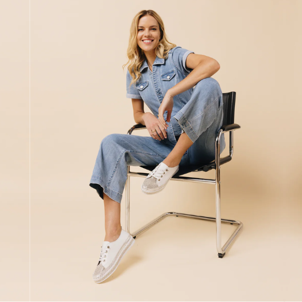 Women in Jean jumper sitting on chair with white rhinestone covered sneakers.