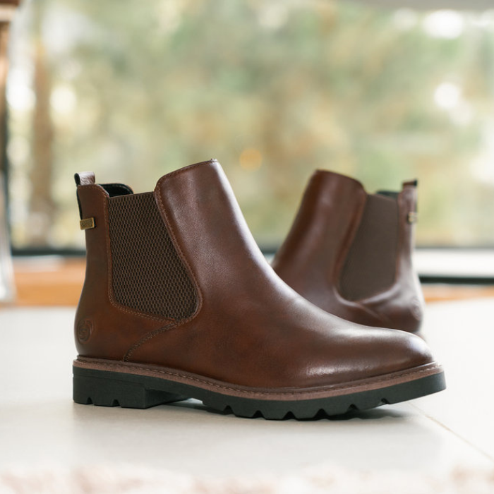 Pair of brown leather Chelsea boots on a light surface with a blurred background.