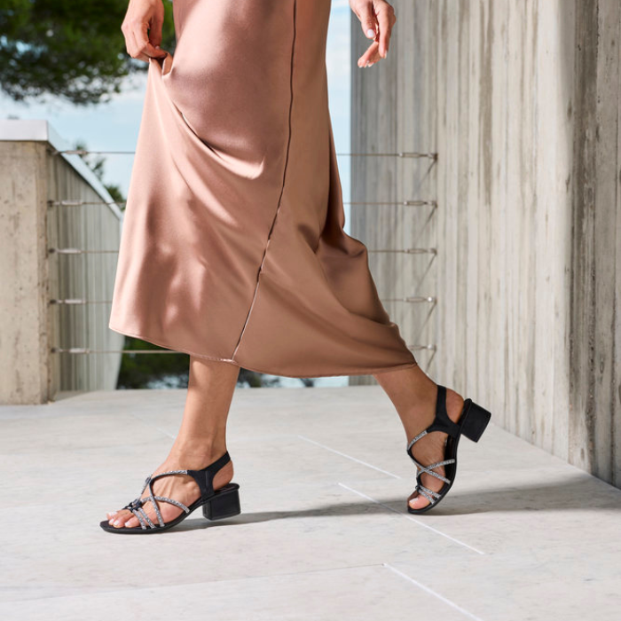 Person wearing a brown dress and black sparkly block heel sandals on a light-colored pavement.