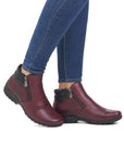 Legs in jeans wearing red ankle boot with black outsole and outside zipper closure.