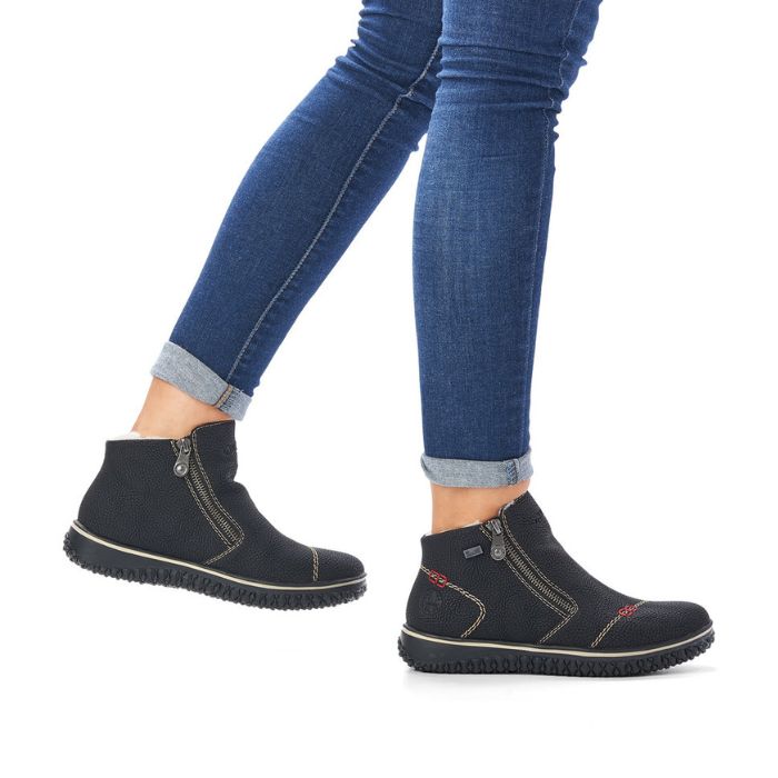 Black ankle boot with grey stitching details, few small red square designs and a front side zipper