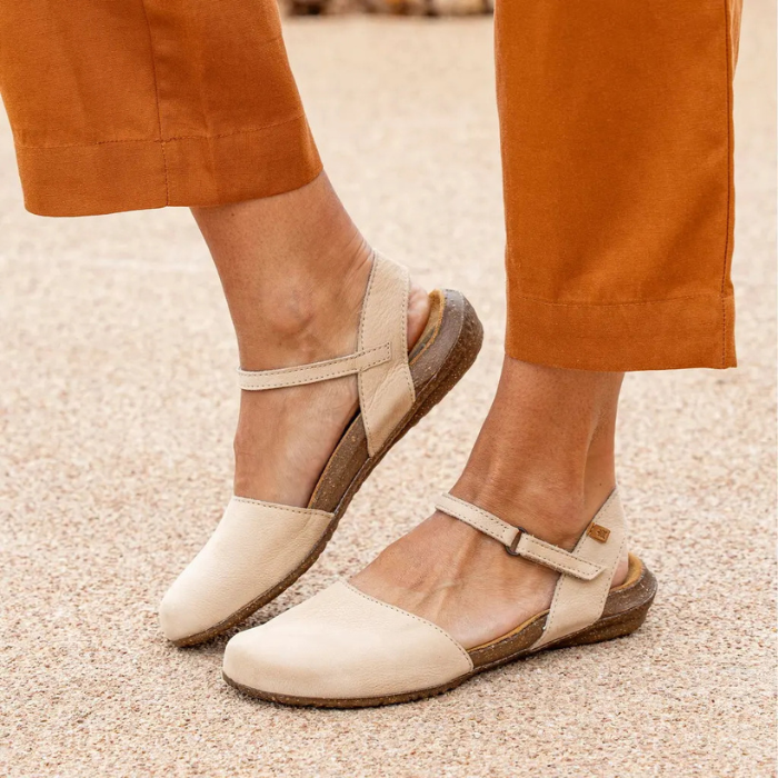 Beige sandals with brown outsoles worn by a person in orange pants.