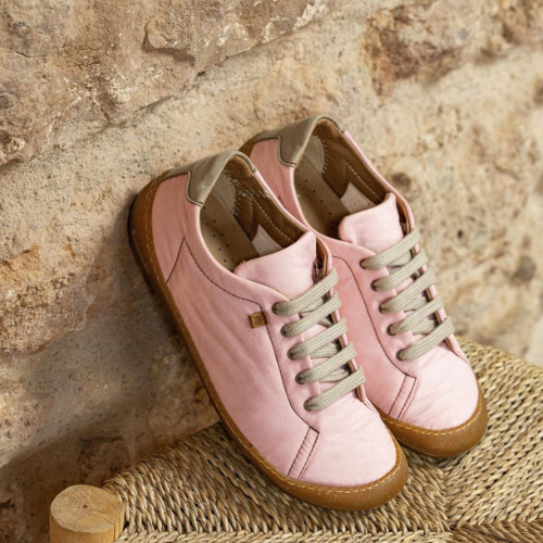 Pair of pink shoes with brown soles on a stone surface.