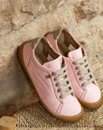 Pair of pink shoes with brown soles on a stone surface.