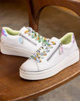 White Remonte D1C06 women's platform sneakers with colorful laces and zipper, displayed on a wooden chair for lifestyle appeal.
