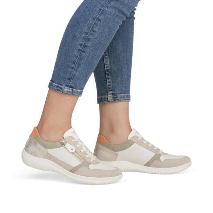 Beige sneakers with green and orange accents worn with blue jeans.