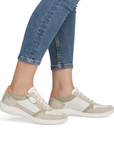 Beige sneakers with green and orange accents worn with blue jeans.