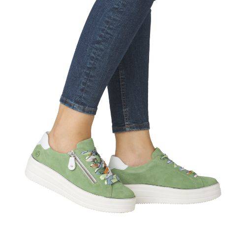 Model wearing green lace-up platform sneakers with colorful laces and white heel, paired with denim jeans.
