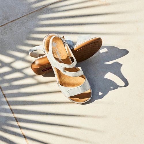 White strappy sandals on concrete with leaf shadows nearby.