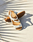 White strappy sandals on concrete with leaf shadows nearby.