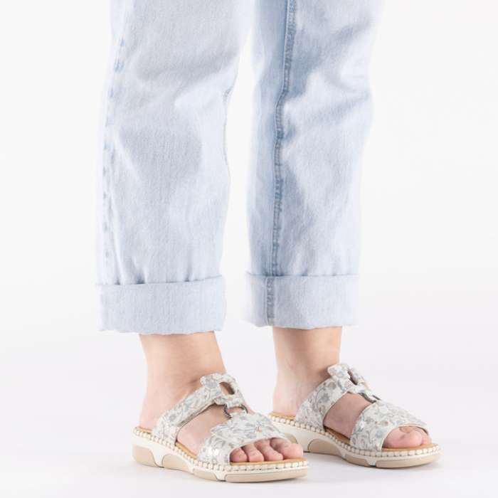 Grey sandals with floral pattern worn with light blue jeans.