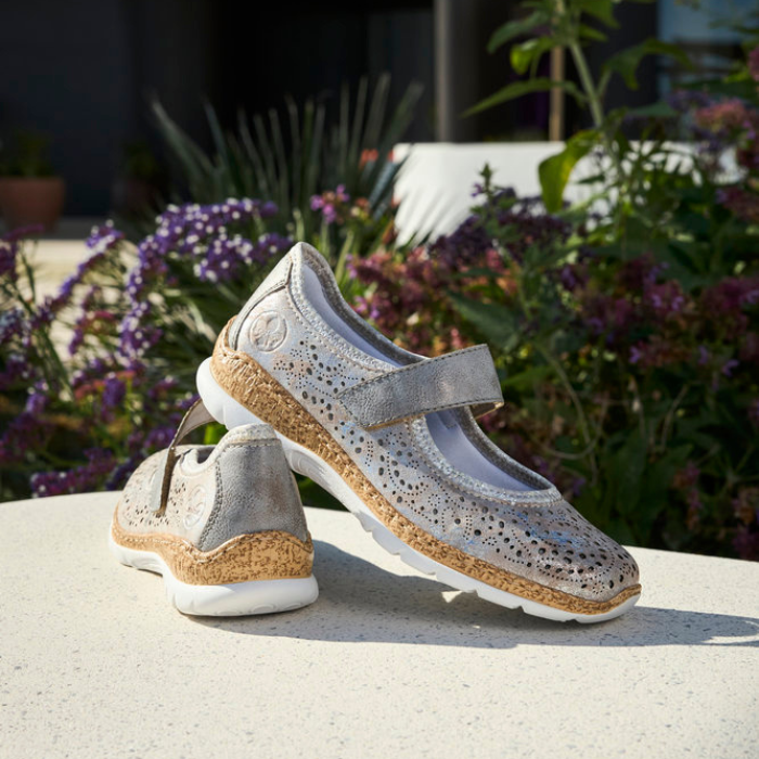 Pair of silver Mary-Jane shoes on a surface with flowers in the background.