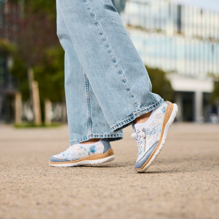 Person wearing white and light blue sneakers with jeans outdoors.