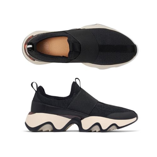 Pair of black slip-on sneakers with a mesh upper, tan footbed. white thick midsole and a black wave pattern rubber outsole.