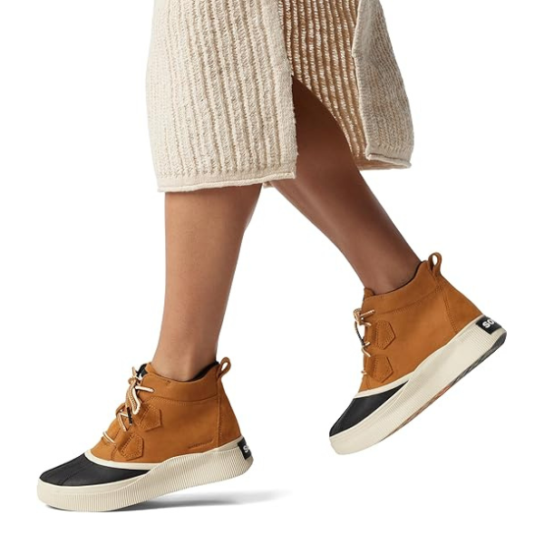 Model wearing tan Sorel Out N About IV Classic waterproof boots with beige skirt, showcasing ankle-high design for rainy day style.