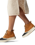 Model wearing tan Sorel Out N About IV Classic waterproof boots with beige skirt, showcasing ankle-high design for rainy day style.