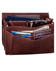 Inside of the brown handbag clutch by Derek Alexander holding many cards, cell phone, pens and money