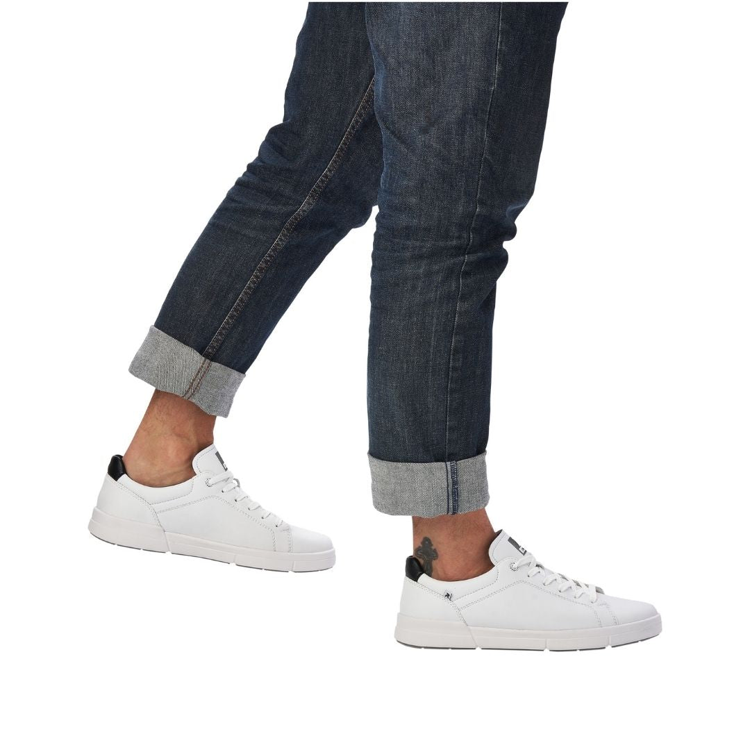 Man in jeans wearing white leather lace up shoes with black heel accent.