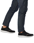 Man in dark jeans wearing a black lace up sneaker with grey accents, white midsole and black outsole.