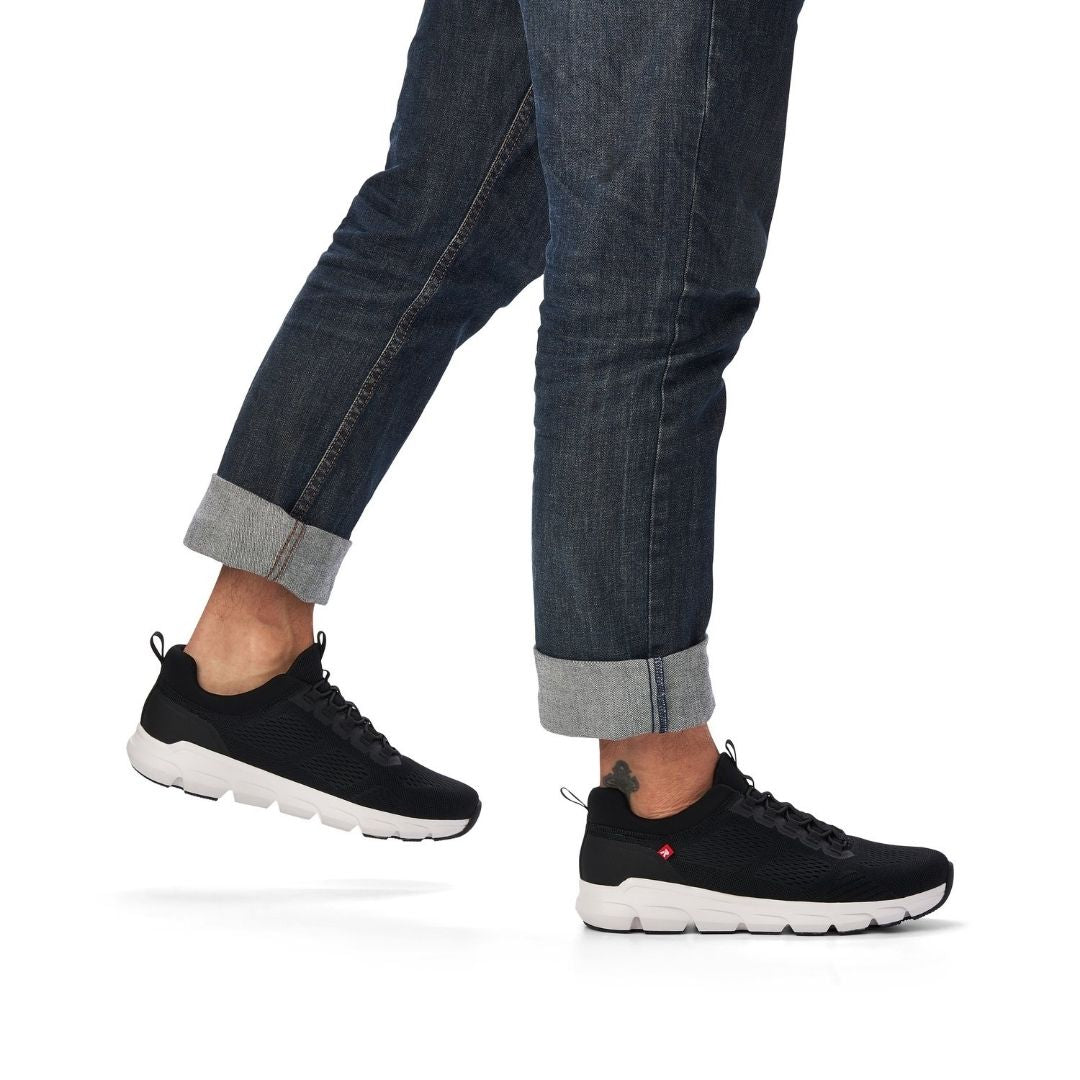 Man in cuffed jeans wearing black slip on sneaker with elastic laces, heel pull tab and white outsole.