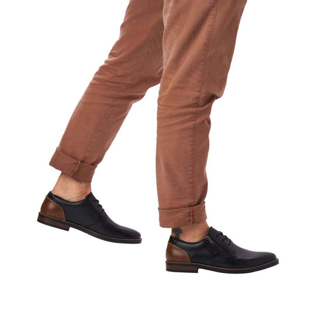 Man in brown pants wearing black leather dress shoes with laces and zipper closure.