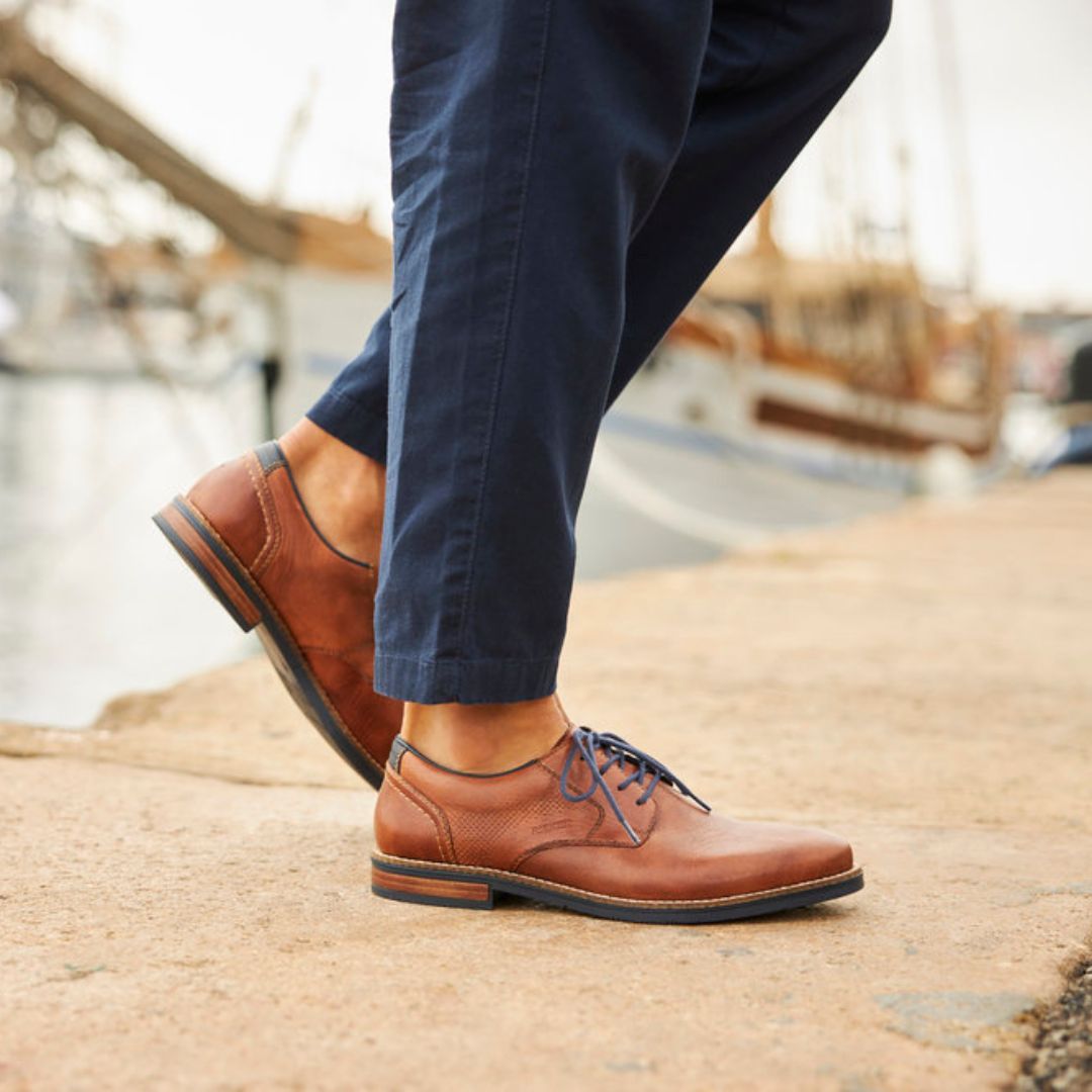Man in navy pants wearing brown leather lace-up shoes with navy laces.