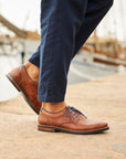 Man in navy pants wearing brown leather lace-up shoes with navy laces.