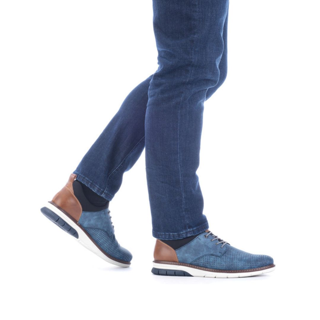Man in jeans wearing blue slip-on sneakers with elastic laces.