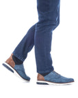 Man in jeans wearing blue slip-on sneakers with elastic laces.