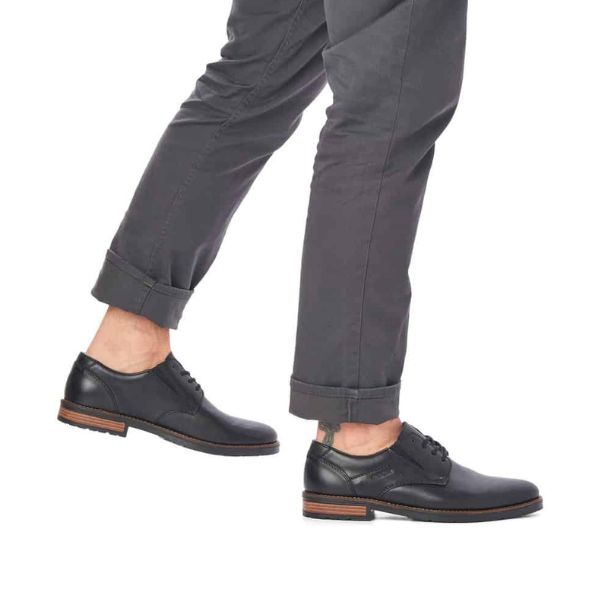 Man in grey pants wearing black leather lace-up Rieker dress shoes.