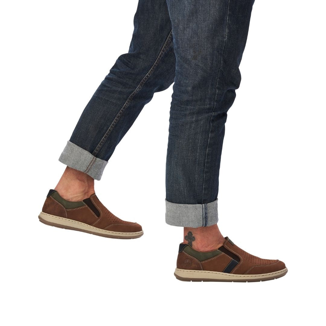 Man in jeans wearing brown slip on shoes with beige midsole and brown outsole.