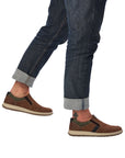 Man in jeans wearing brown slip on shoes with beige midsole and brown outsole.