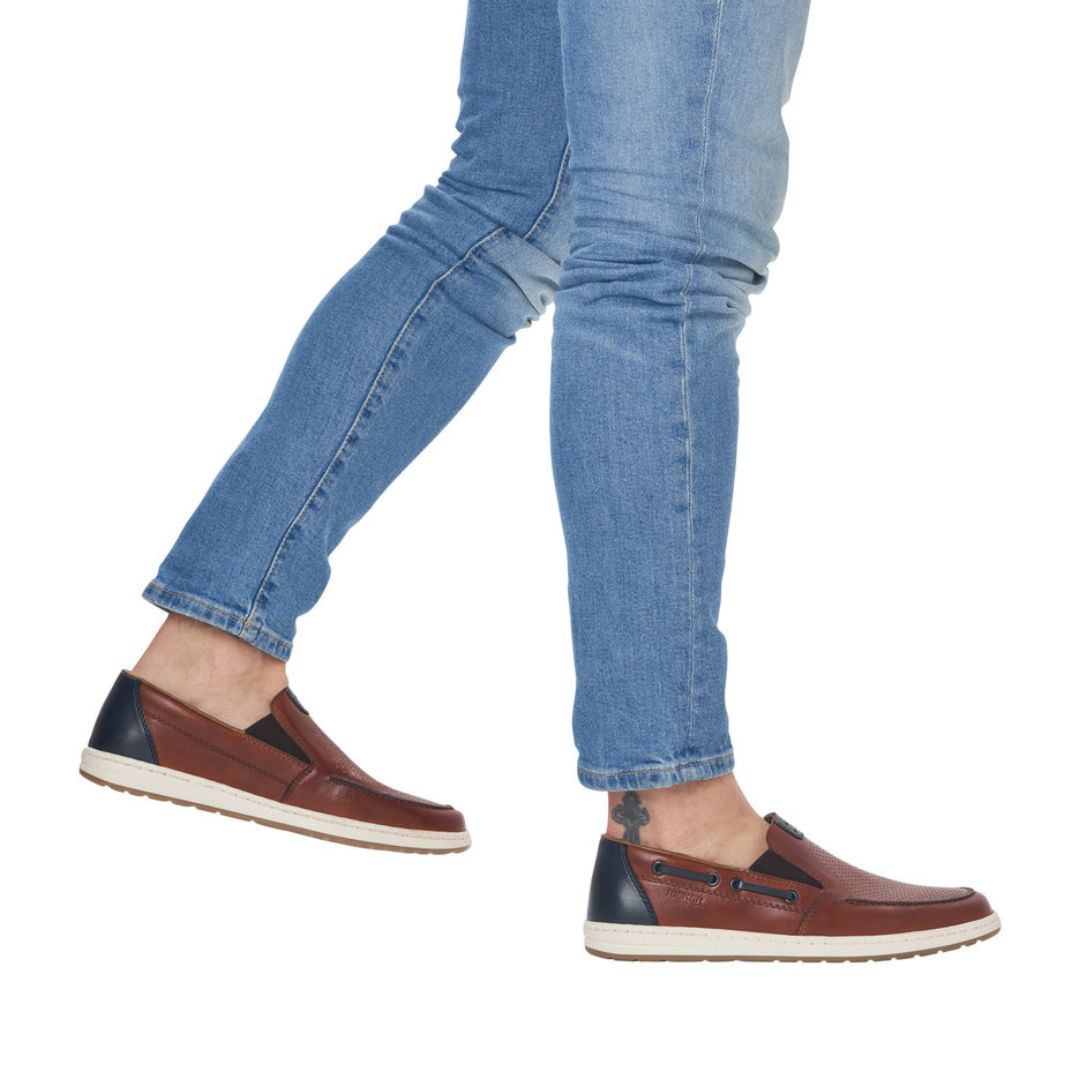 Man in jeans wearing brown leather boat shoes with navy accents, cream midsole and brown outsole.